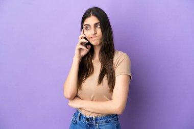 Mor arka planda izole edilmiş cep telefonu kullanan beyaz bir kadın. Şüpheleri ve düşünceleri var.