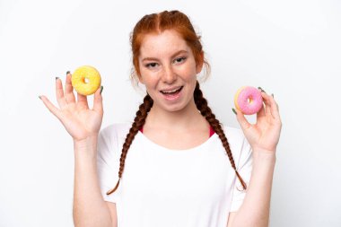 Young reddish woman isolated on white background holding donuts with happy expression