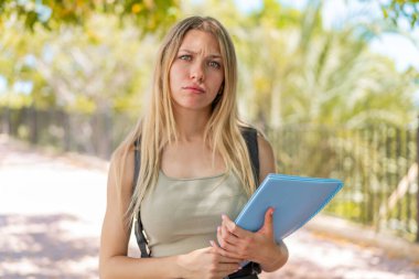 Dışarıda üzgün bir ifadeyle sarışın genç bir bayan öğrenci.