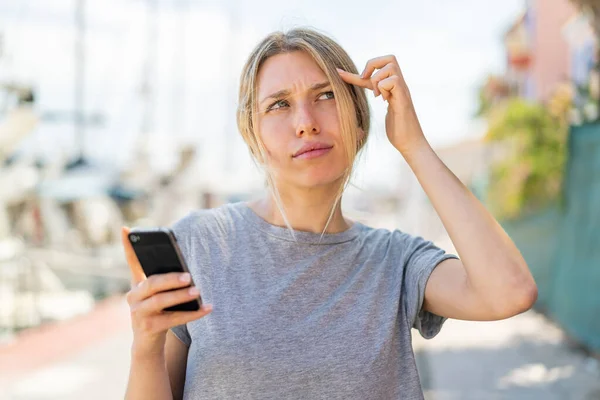 Young Blonde Woman Using Mobile Phone Outdoors Having Doubts Confuse — Stock Photo, Image