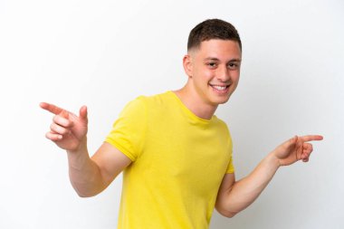 Beyaz arka planda izole edilmiş genç Brezilyalı adam parmak uçlarını işaret ediyor ve mutlu.