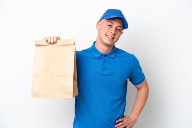 Genç Brezilyalı bir adam beyaz arka planda izole edilmiş bir paket yiyecek alıyor. Kolları kalçasında ve gülümsüyor.