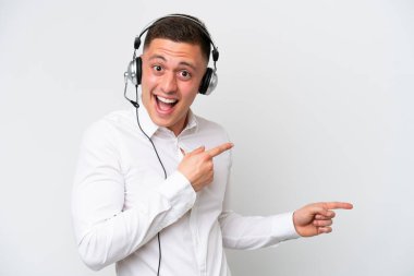 Tele pazarlamacı Brezilyalı adam beyaz arka planda izole edilmiş kulaklıkla çalışıyor. Şaşırmış ve işaret ediyor.