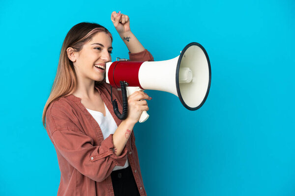 Молодая белая женщина на голубом фоне кричит через мегафон, чтобы объявить что-то в боковом положении