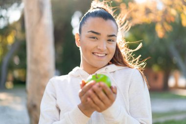 Genç, güzel, spor bir kadın elinde mutlu bir ifadeyle bir elma tutuyor.