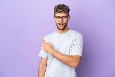 Mor arka planda izole edilmiş beyaz adam şaşırmış ve işaret ediyor.