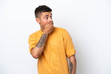 Beyaz arka planda izole edilmiş beyaz Brezilyalı genç bir adam yan tarafa bakarken sürpriz jest yapıyor.