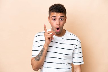 Bej arka planda izole edilmiş genç Brezilyalı bir adam parmağını kaldırarak çözümü anlamaya çalışıyor.