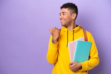 Young student Brazilian man isolated on purple background pointing to the side to present a product