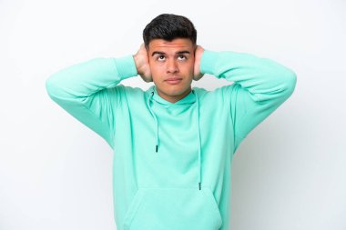 Beyaz arka planda izole edilmiş beyaz, yakışıklı genç adam hayal kırıklığına uğramış ve kulaklarını kapatmış.