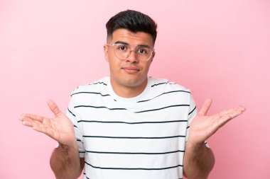 Pembe arka planda izole edilmiş, gözlüklü ve kuşkusu olan beyaz tenli yakışıklı bir genç.