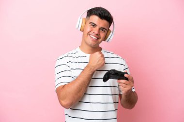 Pembe arka planda izole edilmiş bilgisayar oyunu kontrolörüyle oynayan yakışıklı genç bir adam zaferi kutluyor.