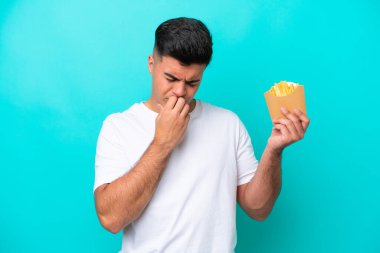 Young caucasian man catching french fries isolated on blue background having doubts