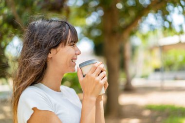 Açık havada elinde kahve tutan genç bir kadın.