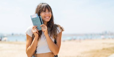 Açık havada elinde mutlu bir ifadeyle pasaport tutan genç bir kadın.