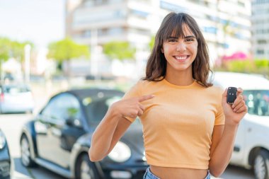 Dışarıda arabanın anahtarlarını tutan genç bir kadın. Sürpriz bir yüz ifadesi var.