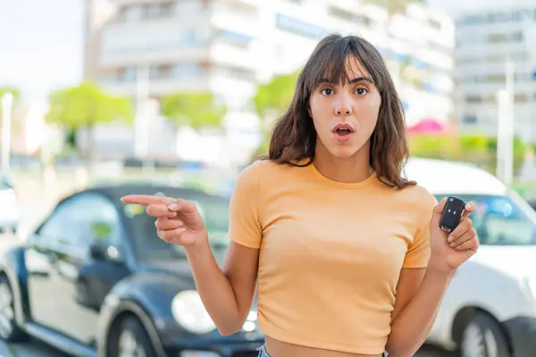 屋外で車の鍵を握っている若い女性は驚き 側面を指す — ストック写真