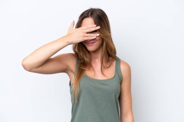 Beyaz arka planda soyutlanmış beyaz tenli genç bir kadın elleriyle gözlerini kapatıyor ve gülümsüyor.