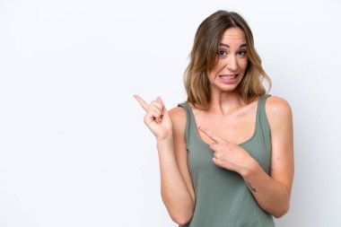 Beyaz arka planda izole edilmiş genç beyaz bir kadın korkmuş ve kenarı işaret ediyor.