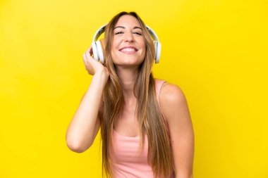 Sarı arka planda izole edilmiş genç beyaz kadın müzik dinliyor.