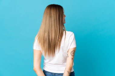 Genç Slovak kadın mavi arka planda izole edilmiş ve arkasına bakıyor.