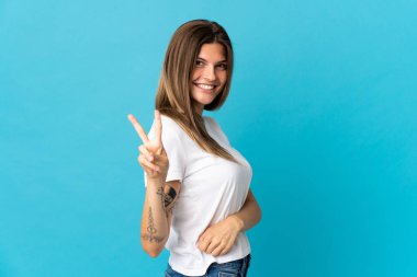 Mavi arka planda izole edilmiş genç Slovak kadın gülümsüyor ve zafer işareti gösteriyor.