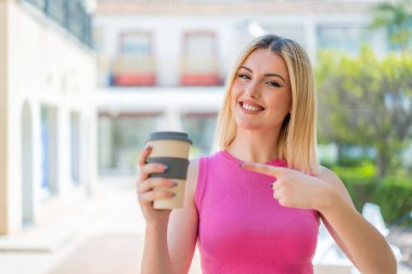 Genç, güzel, sarışın kadın açık havada ve onu işaret ediyor.