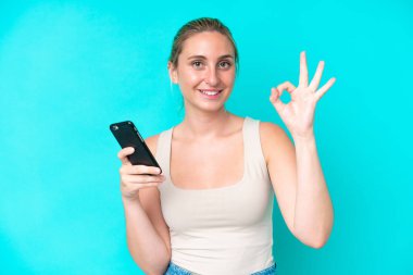 Genç beyaz kadın mavi arka planda izole edilmiş ve cep telefonu kullanıyor.