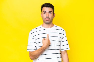 Soyutlanmış sarı arka planı olan yakışıklı genç bir adam kendini işaret ediyor.