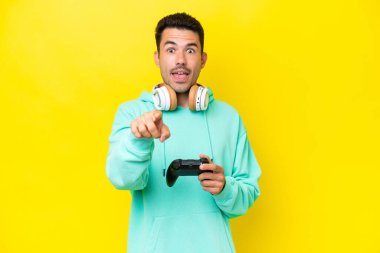 Bir video oyunu kontrolörüyle oynayan yakışıklı genç bir adam tecrit edilmiş duvarın üzerinde şaşırmış ve ön tarafı işaret ediyor.