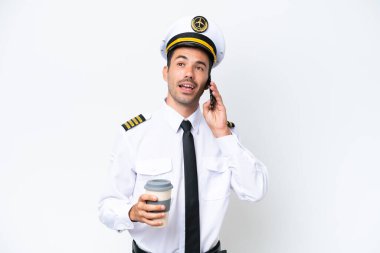 İzole edilmiş beyaz arka plan üzerinde uçak pilotu kahve ve bir cep telefonu tutuyor.