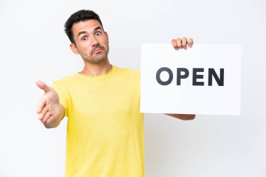 İzole edilmiş beyaz arka planda genç yakışıklı bir adam. Elinde bir pankart tutuyor ve anlaşma yapıyor.