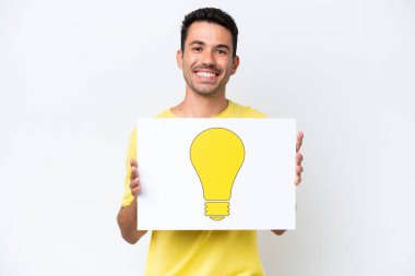 İzole edilmiş beyaz arka plan üzerinde genç yakışıklı bir adam elinde mutlu ifadeli bir ampul simgesi olan bir levha tutuyor.