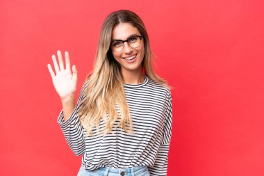 Genç Uruguaylı kadın kırmızı arka planda izole edilmiş mutlu bir ifadeyle selamlıyor.