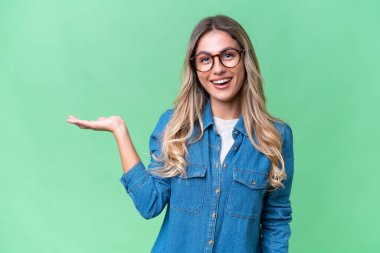 Genç Uruguaylı kadın, izole edilmiş arka planda bir ilan vermek için avucunun içinde hayali bir mekan tutuyor.