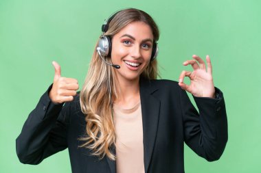 Tele pazarlamacı güzel Uruguaylı kadın izole bir arka planda çalışan tamam işareti ve baş parmak hareketi gösteren bir kulaklıkla