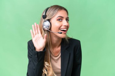 Tele pazarlamacı güzel Uruguaylı bir kadın izole bir arka planda çalışan bir kulaklıkla bir şeyler dinlerken elini kulağına koyuyor.