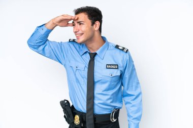 Young police caucasian man isolated on white background looking far away with hand to look something