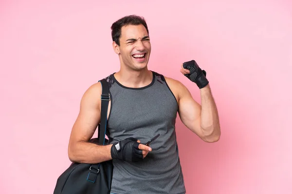 Young sport caucasian man with sport bag isolated on pink background with phone in victory position