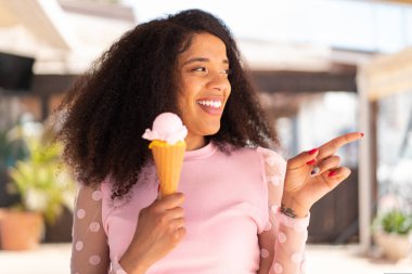 Açık havada kornet dondurması olan genç Afrikalı Amerikalı kadın bir ürünü sunmak için yan tarafı işaret ediyor.
