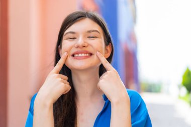 Açık havada gülümseyen genç ve güzel bir kadın. Mutlu ve hoş bir ifadeyle.