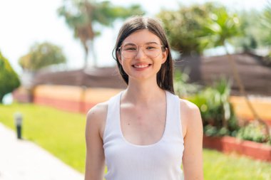 Genç, güzel bir kadın açık havada, neşeli bir gözlüğü var.