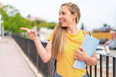 Açık havada genç sarışın bir bayan bir ürün sunmak için kenarı işaret ediyor.