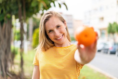 Açık havada elinde portakal tutan genç sarışın kadın.