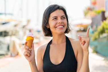 Açık havada kornet dondurması olan genç ve güzel Bulgar kadın, çözümün farkına varmak için parmağını kaldırıyor.