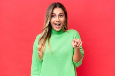 Genç Uruguaylı kadın kırmızı arka planda izole edilmiş şaşırmış ve ön tarafı işaret ediyor.