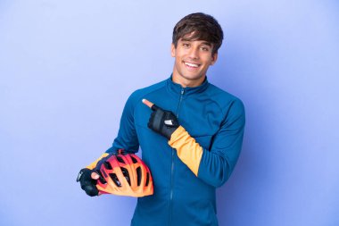 Mor arka planda izole edilmiş genç bir beyaz adam bir ürünü sunmak için yan tarafı işaret ediyor.