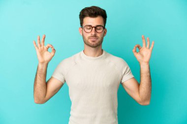 Beyaz tenli yakışıklı adam, mavi arka planda Zen pozuyla izole edilmiş.