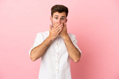 Young caucasian handsome man isolated on pink background covering mouth with hands