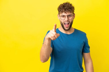 Sarı arka planda izole edilmiş yakışıklı beyaz adam hayal kırıklığına uğramış ve ön tarafı işaret ediyor.
